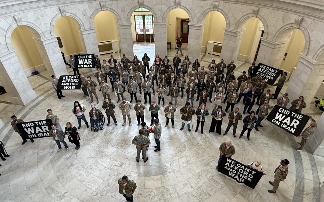 Veterans standing in formation in the Cannon House Office Building rotunda, holding red tulips and folded flags.